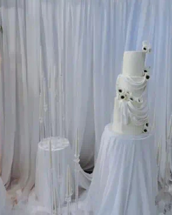 Tall white multi-tier wedding cake on a draped table